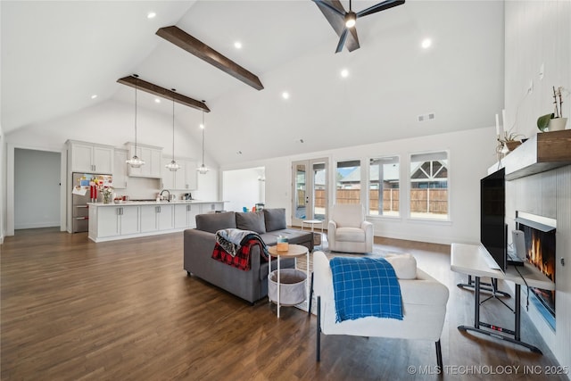 living room with a warm lit fireplace, visible vents, dark wood finished floors, high vaulted ceiling, and beam ceiling