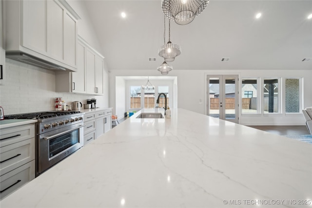 kitchen featuring a sink, vaulted ceiling, french doors, high end stainless steel range oven, and an inviting chandelier