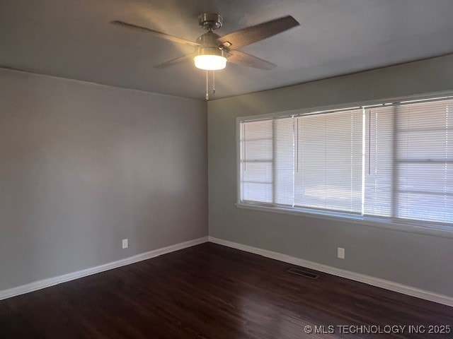 empty room with baseboards, visible vents, ceiling fan, and dark wood-style flooring