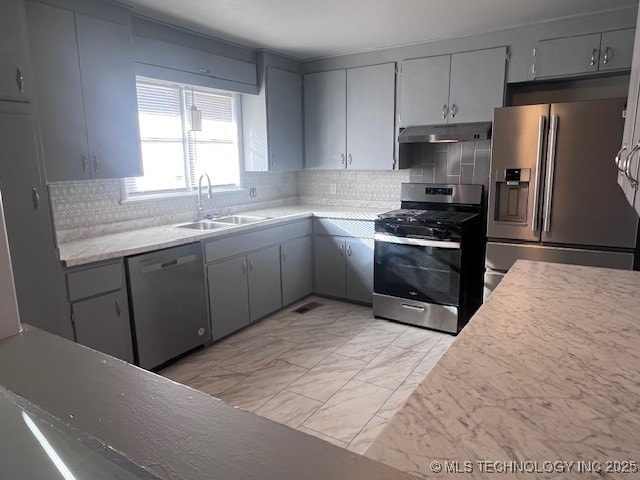 kitchen featuring appliances with stainless steel finishes, marble finish floor, gray cabinets, under cabinet range hood, and a sink