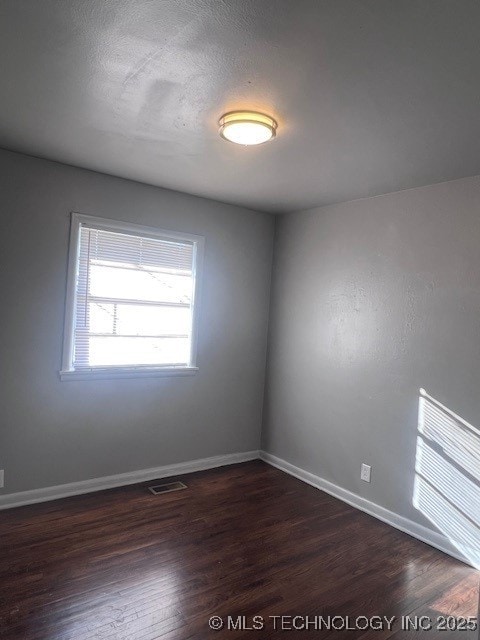 empty room featuring a textured ceiling, dark wood-style flooring, visible vents, and baseboards