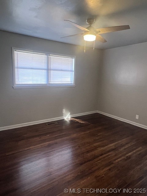 spare room with dark wood-style flooring, visible vents, ceiling fan, and baseboards