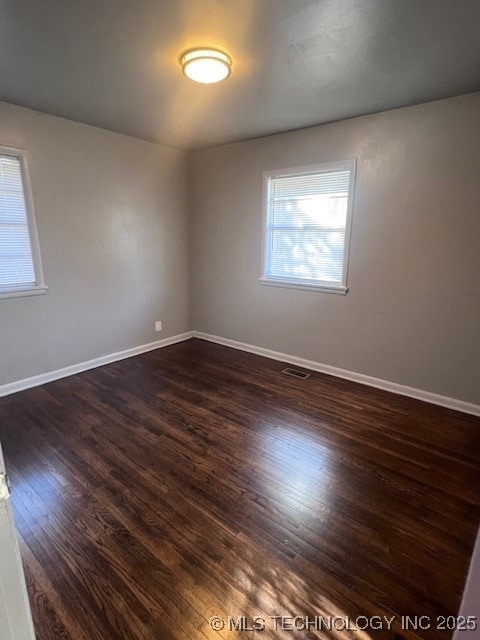 unfurnished room with dark wood-style flooring, visible vents, and baseboards