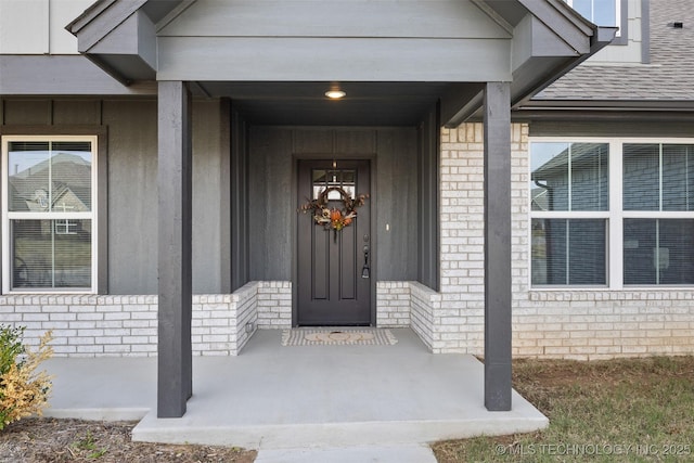 entrance to property featuring a shingled roof and brick siding