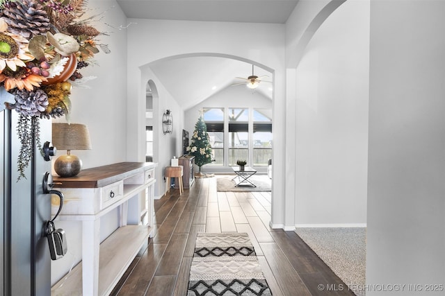 hall with baseboards, arched walkways, vaulted ceiling, and wood finish floors