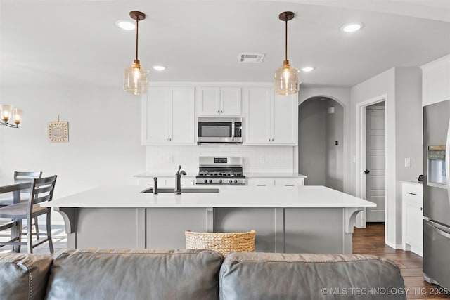 kitchen featuring stainless steel appliances, tasteful backsplash, visible vents, dark wood-type flooring, and a sink