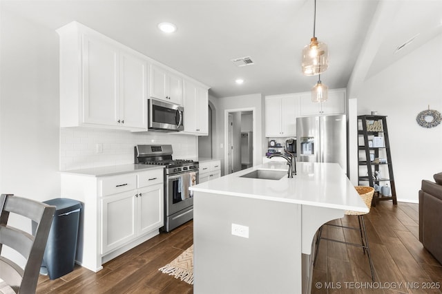 kitchen featuring stainless steel appliances, a breakfast bar, a sink, backsplash, and dark wood-style floors