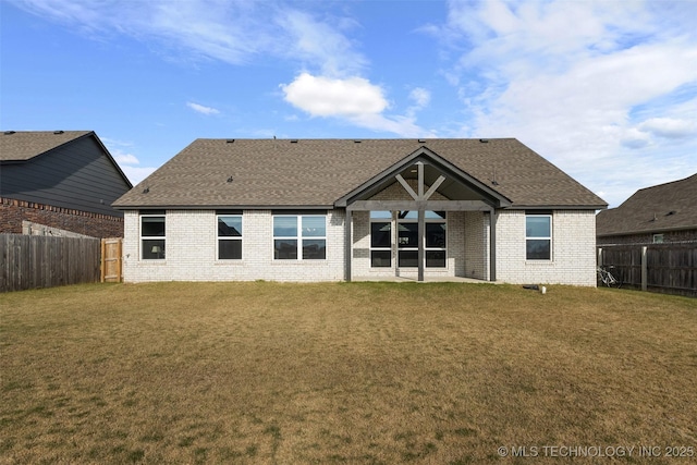 back of property featuring brick siding, a fenced backyard, a shingled roof, and a yard