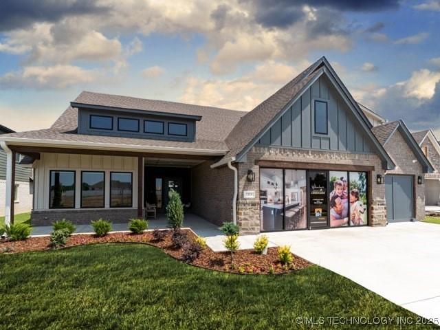 view of front of house with an attached garage, brick siding, driveway, a front lawn, and board and batten siding