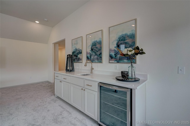 bar featuring lofted ceiling, light carpet, a sink, beverage cooler, and baseboards