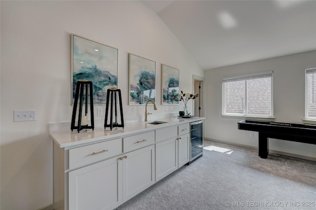 bar featuring light carpet, baseboards, wine cooler, vaulted ceiling, and a sink