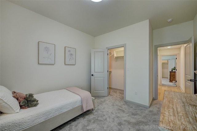 bedroom with a closet, light carpet, a spacious closet, and baseboards