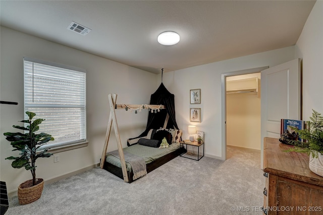 carpeted bedroom featuring a walk in closet, visible vents, and baseboards