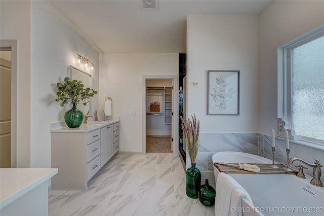 full bathroom featuring a walk in closet, marble finish floor, visible vents, vanity, and a freestanding tub