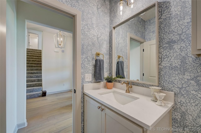 bathroom with wallpapered walls, baseboards, wood finished floors, and vanity