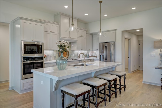 kitchen featuring appliances with stainless steel finishes, a sink, light countertops, light wood-type flooring, and backsplash