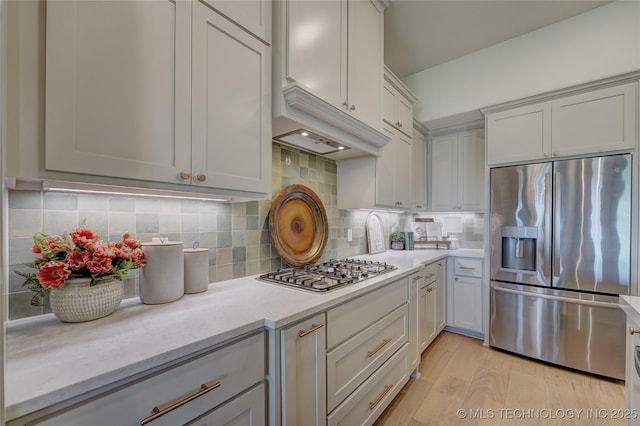 kitchen with stainless steel appliances, tasteful backsplash, light wood-style flooring, and light stone counters