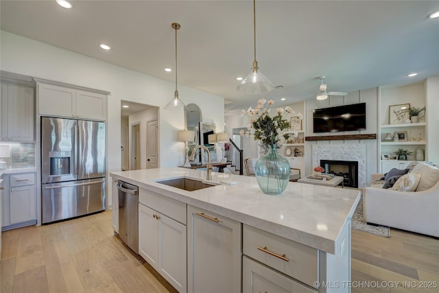 kitchen featuring a fireplace, light wood finished floors, stainless steel appliances, open floor plan, and a sink