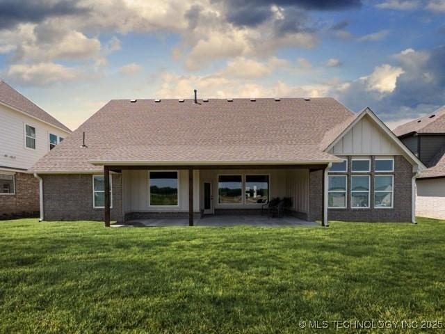 rear view of property with a patio area, roof with shingles, a lawn, and brick siding