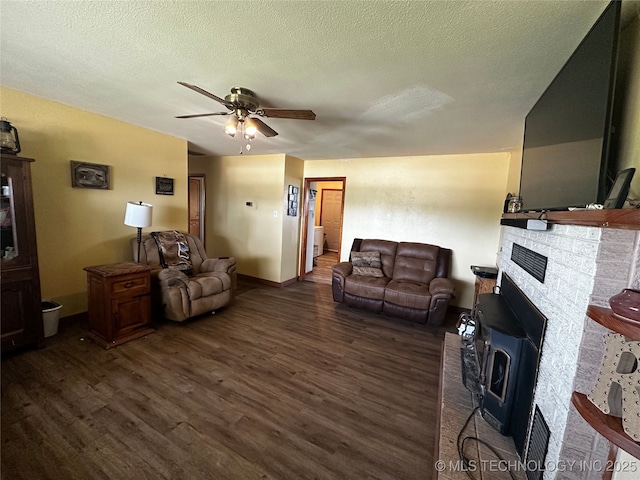 living room with ceiling fan, dark wood-style flooring, a textured ceiling, and a wood stove