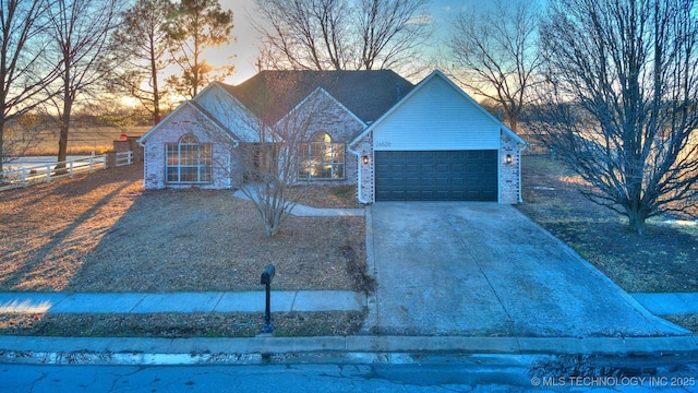 view of front facade with a garage, concrete driveway, brick siding, and fence