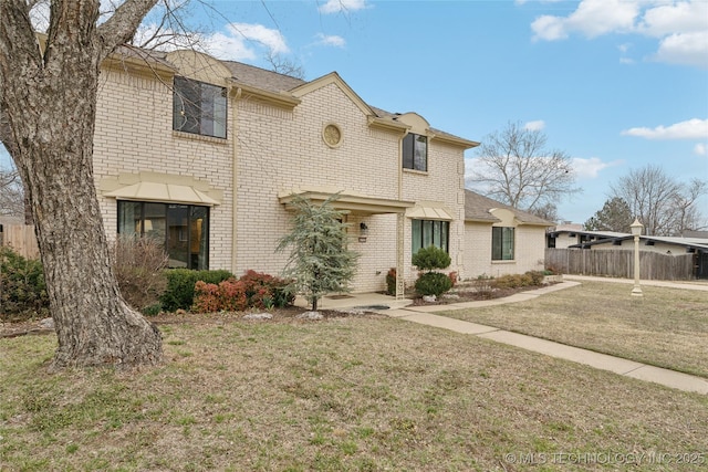 view of front facade featuring brick siding, fence, and a front yard