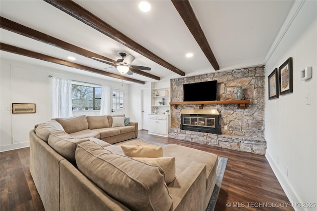 living area featuring ceiling fan, a fireplace, baseboards, beam ceiling, and dark wood finished floors