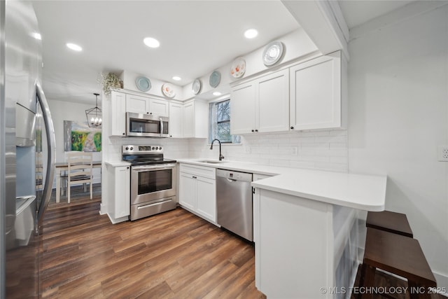 kitchen featuring white cabinets, dark wood-type flooring, a peninsula, stainless steel appliances, and a sink