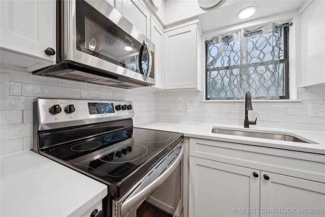 kitchen with stainless steel appliances, light countertops, backsplash, white cabinets, and a sink