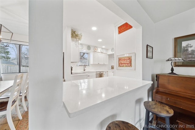 kitchen featuring light countertops, white cabinets, a sink, dishwasher, and a kitchen breakfast bar