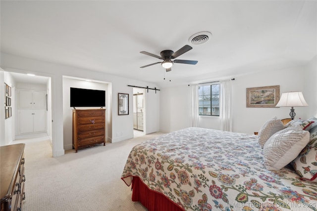 bedroom featuring ensuite bathroom, a barn door, light carpet, visible vents, and baseboards