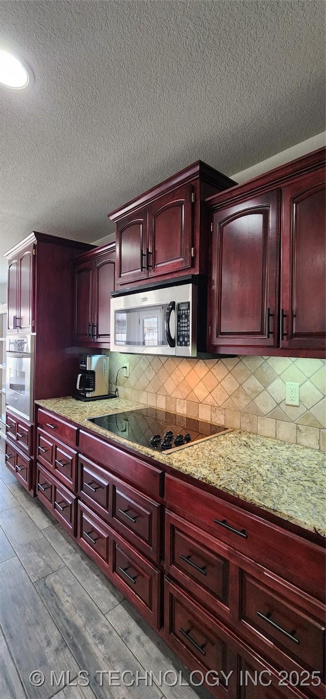 kitchen with tasteful backsplash, dark brown cabinets, appliances with stainless steel finishes, and light stone counters