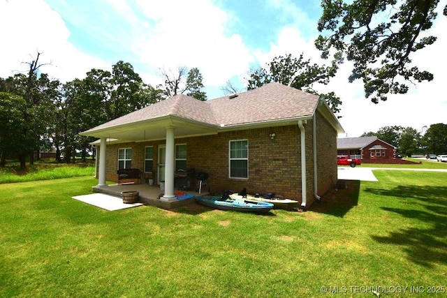 back of house with a shingled roof, brick siding, a patio, and a lawn