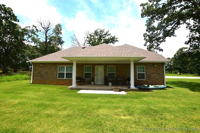 rear view of house with a yard, a shingled roof, a patio area, and brick siding