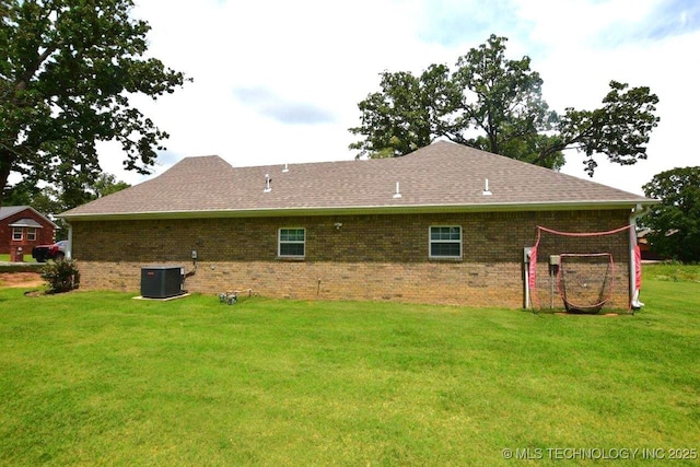 rear view of property featuring central AC, a lawn, brick siding, and roof with shingles