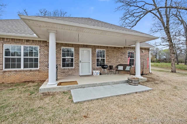 exterior space with a patio area, roof with shingles, and brick siding