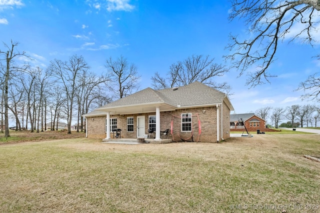 back of property featuring brick siding, a shingled roof, a porch, and a yard