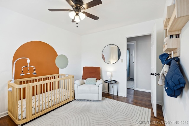 bedroom featuring a nursery area, a ceiling fan, baseboards, and wood finished floors