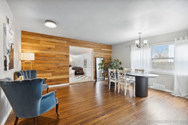 dining area with a notable chandelier, visible vents, wood walls, and wood finished floors