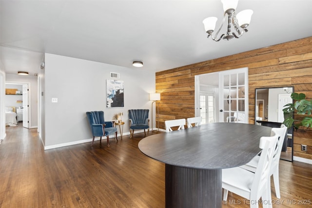 dining area with wooden walls, french doors, an inviting chandelier, and dark wood-style flooring