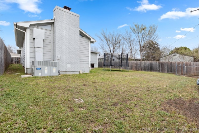 rear view of house featuring a trampoline, a lawn, a fenced backyard, and a chimney