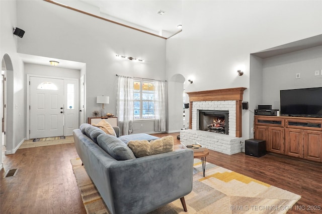 living room featuring arched walkways, visible vents, a brick fireplace, and wood finished floors