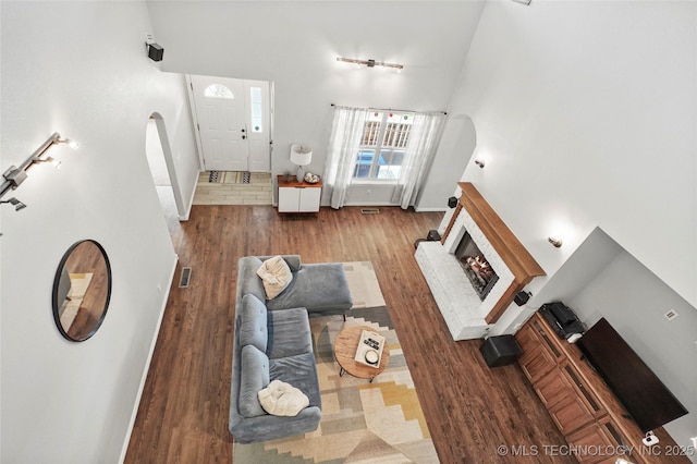 living room featuring a high ceiling, a brick fireplace, wood finished floors, and arched walkways