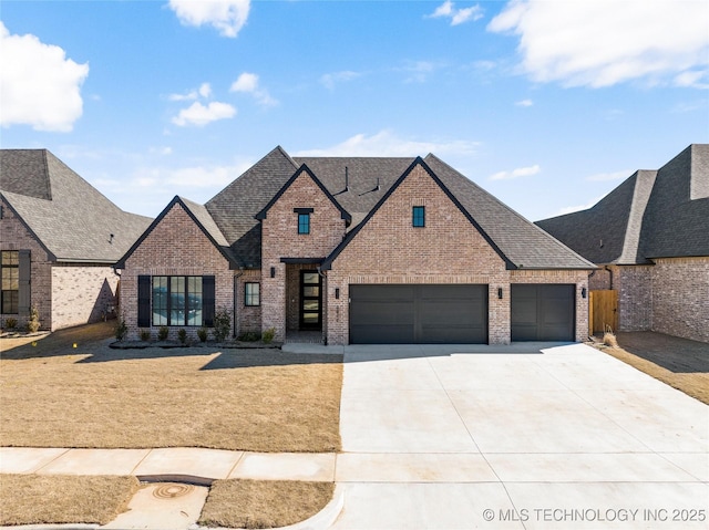 french country style house with driveway, roof with shingles, and brick siding