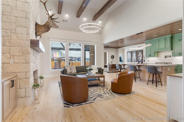 living area featuring light wood finished floors, visible vents, a fireplace, high vaulted ceiling, and beam ceiling