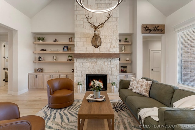 living room featuring high vaulted ceiling, a fireplace, baseboards, built in features, and light wood finished floors