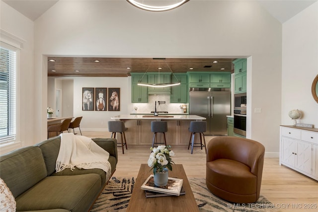 living area with high vaulted ceiling, a healthy amount of sunlight, light wood-style flooring, and baseboards