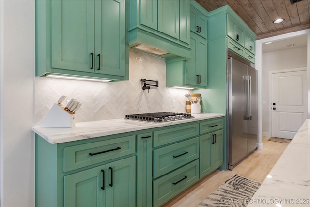 kitchen with light stone counters, stainless steel appliances, custom exhaust hood, tasteful backsplash, and green cabinetry