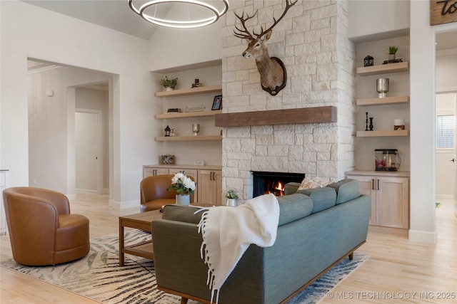 living room with light wood-style flooring, built in shelves, baseboards, and a stone fireplace