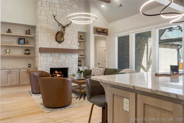 living area featuring high vaulted ceiling, a fireplace, visible vents, and light wood-style floors